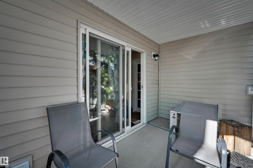 Covered patio featuring a sliding glass door, exterior siding, and an attached wall light - #203 24 Alpine Pl, St. Albert, AB 