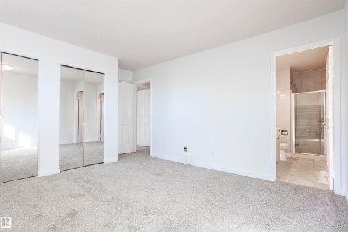 Wall-to-wall carpeting, mirrored closet doors, white walls, white trim, and an adjacent bathroom with a glass-enclosed shower - 17927 80 Avenue Nw, Edmonton, AB 