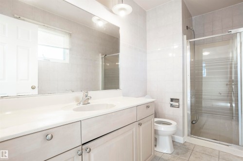 Vanity with integrated sink, glass-enclosed shower, tiled walls, and window with blinds - 17927 80 Avenue Nw, Edmonton, AB 