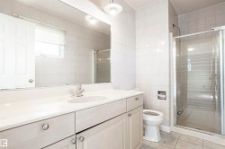 Vanity with integrated sink, glass-enclosed shower, tiled walls, and window with blinds - 