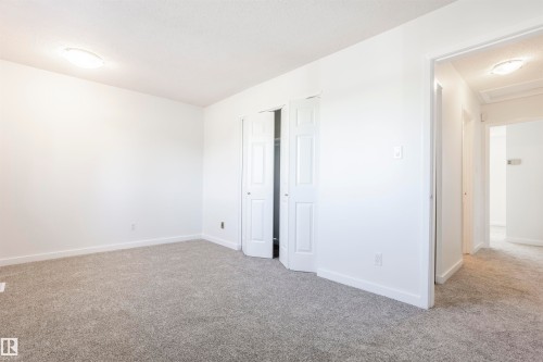 Neutral tone wall paint, grey carpet flooring, white trim, and bi-fold closet doors - 17927 80 Avenue Nw, Edmonton, AB 