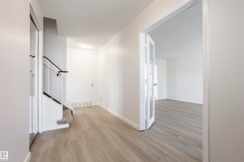 Wood-finish flooring, white walls, flush mount lighting, a staircase with carpeting, and glass-paneled French doors - 17927 80 Avenue Nw, Edmonton, AB 