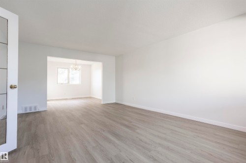 Expansive room with light wood-finish flooring, white walls, and a wide entryway to an additional space - 17927 80 Avenue Nw, Edmonton, AB 