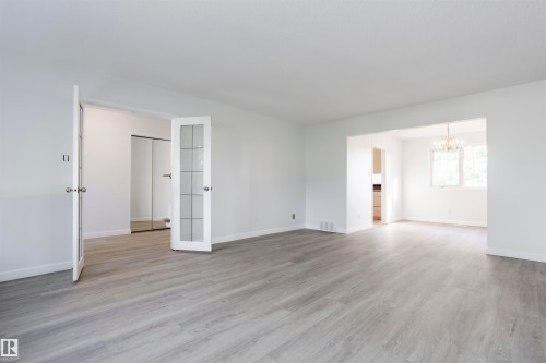 Light wood-finish flooring throughout, white walls, double French doors with frosted glass panels, an arched doorway, and a chandelier in the adjacent space - 17927 80 Avenue Nw, Edmonton, AB 