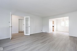Light wood-finish flooring throughout, white walls, double French doors with frosted glass panels, an arched doorway, and a chandelier in the adjacent space - 