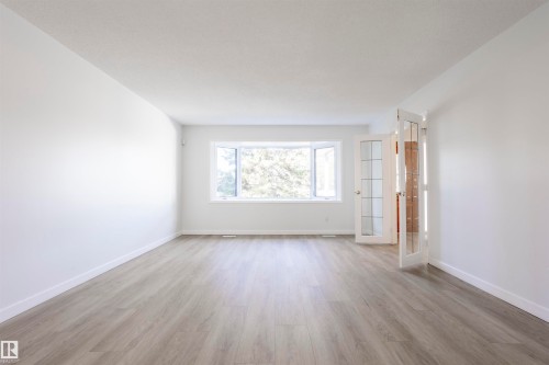 Expansive room featuring wood-finish flooring, white walls, a large bay window, and French doors with glass panels - 17927 80 Avenue Nw, Edmonton, AB 