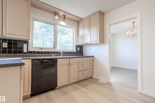 Kitchen featuring light-toned cabinetry, dark countertops, black subway tile backsplash, and wood-finish flooring - 17927 80 Avenue Nw, Edmonton, AB 