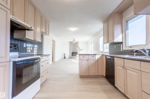 Light-toned cabinetry, dark tile backsplash, wood-finish flooring, and a stone-clad fireplace - 17927 80 Avenue Nw, Edmonton, AB 