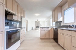 Light-toned cabinetry, dark tile backsplash, wood-finish flooring, and a stone-clad fireplace - 