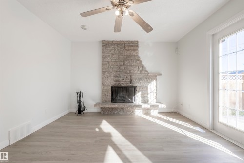 Stone-clad fireplace with hearth, wood-finish flooring, ceiling fan with integrated lighting, and a glass-paneled exterior door - 17927 80 Avenue Nw, Edmonton, AB 