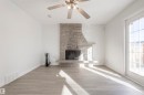 Stone-clad fireplace with hearth, wood-finish flooring, ceiling fan with integrated lighting, and a glass-paneled exterior door - 17927 80 Avenue Nw, Edmonton, AB 