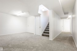 Spacious lower-level room featuring light gray carpeting, white walls, and bright overhead lighting - 