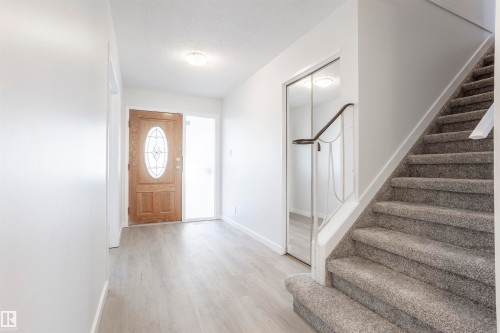 Wood-finish flooring in the entryway with a wood front door featuring an oval decorative glass insert - 17927 80 Avenue Nw, Edmonton, AB 