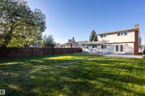 Expansive lawn area with a perimeter privacy fence, mature trees, and a concrete patio - 17927 80 Avenue Nw, Edmonton, AB 
