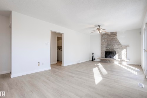 Spacious living area featuring light wood-finish flooring, a stone-clad fireplace, and a ceiling fan - 17927 80 Avenue Nw, Edmonton, AB 