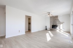 Spacious living area featuring light wood-finish flooring, a stone-clad fireplace, and a ceiling fan - 