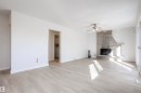 Spacious living area featuring light wood-finish flooring, a stone-clad fireplace, and a ceiling fan - 17927 80 Avenue Nw, Edmonton, AB 