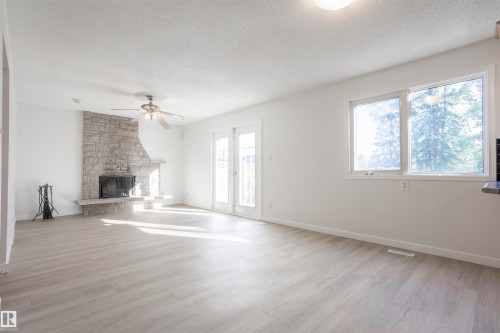 Stone-clad fireplace with hearth, wood-finish flooring, white walls, ceiling fan, and French doors - 17927 80 Avenue Nw, Edmonton, AB 