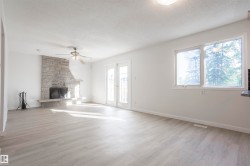 Stone-clad fireplace with hearth, wood-finish flooring, white walls, ceiling fan, and French doors - 