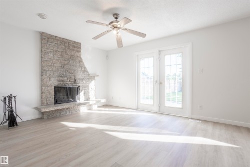 Stone fireplace with a hearth, ceiling fan, and light wood-finish flooring - 17927 80 Avenue Nw, Edmonton, AB 