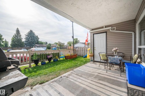 Covered concrete patio with a white entry door, light brown siding, and white downspout - 15017 26 Street Nw, Edmonton, AB 