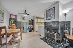 Wood-finish flooring, ceiling fan, and a fireplace with a dark stone surround and hearth - 