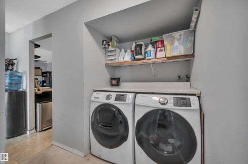 Dedicated laundry area featuring a built-in countertop, open shelving, and tile flooring - 15017 26 Street Nw, Edmonton, AB 