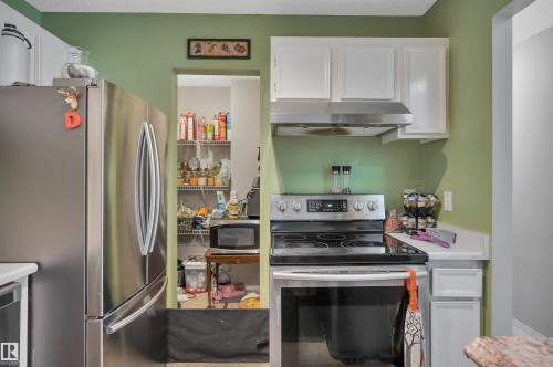 Stainless steel refrigerator, stainless steel range with overhead ventilation, white cabinetry, and a pantry with wire shelving - 15017 26 Street Nw, Edmonton, AB 