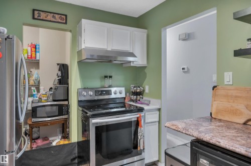 Stainless steel range with coordinating range hood, white upper cabinetry, and a refrigerator - 15017 26 Street Nw, Edmonton, AB 