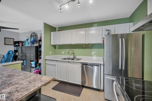 Kitchen featuring white cabinetry, light-toned countertops, a stainless steel dishwasher, and a stainless steel refrigerator - 15017 26 Street Nw, Edmonton, AB 