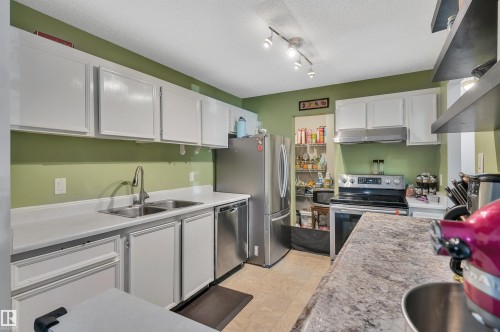 White cabinetry with brushed nickel hardware, a double basin stainless steel sink, stainless steel appliances, and track lighting - 15017 26 Street Nw, Edmonton, AB 