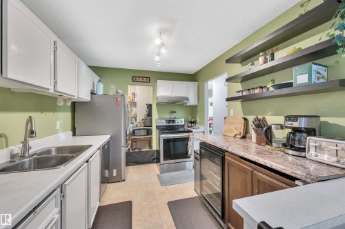 White cabinetry, stainless steel appliances, dual basin sink, light-toned flooring, and open shelving - 15017 26 Street Nw, Edmonton, AB 