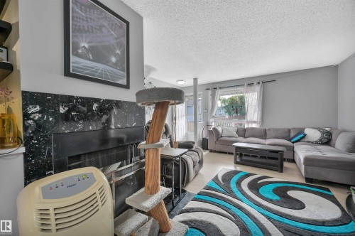 Living area featuring a black mantel with a stone-finish surround, a large window with drapes, and a dropped ceiling - 15017 26 Street Nw, Edmonton, AB 