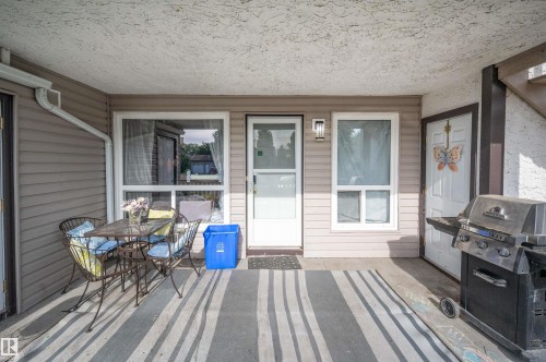 Covered patio featuring a striped outdoor rug, exterior lighting fixture, and a white entry door - 15017 26 Street Nw, Edmonton, AB 