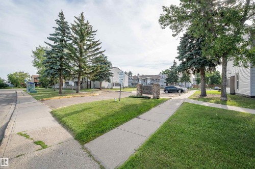 Manicured lawn with mature evergreen trees, concrete sidewalks, and a stone monument - 15017 26 Street Nw, Edmonton, AB 