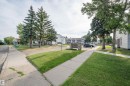 Manicured lawn with mature evergreen trees, concrete sidewalks, and a stone monument - 15017 26 Street Nw, Edmonton, AB 