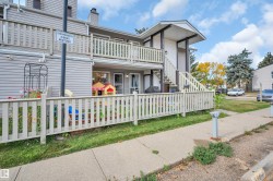 Siding exterior with a white picket fence, concrete sidewalk, and a second-story balcony - 