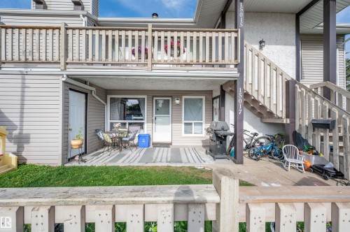 Ground-level patio with direct access to interior, upper-level balcony with wood railing, wood exterior stairs, and light-toned siding - 15017 26 Street Nw, Edmonton, AB 