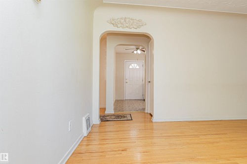 Hardwood flooring, arched doorway with decorative molding, white interior walls, white paneled door with fanlight, and ceiling fan - 8743 Strathearn Drive Nw, Edmonton, AB 