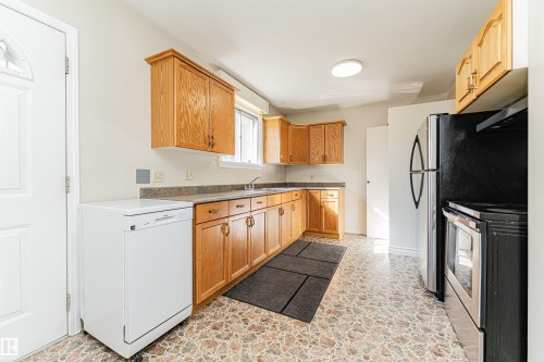 Functional kitchen featuring wood cabinetry, stone-look countertops, and included refrigerator, stove, and dishwasher - 8743 Strathearn Drive Nw, Edmonton, AB 