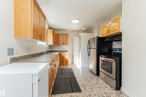 Kitchen featuring wood cabinetry, stone-look countertops, a stainless steel refrigerator, and a stainless steel range - 8743 Strathearn Drive Nw, Edmonton, AB 