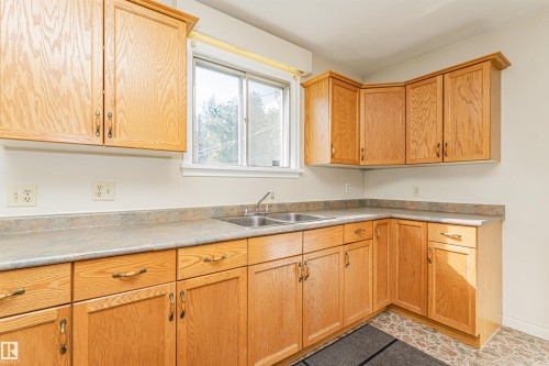 U-shaped kitchen layout with wood-finish cabinetry, a double basin stainless steel sink, and a light-toned countertop - 8743 Strathearn Drive Nw, Edmonton, AB 
