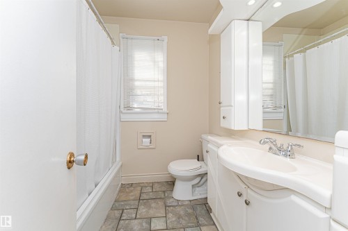 Bathroom with a vanity sink, built-in storage cabinet, mirror, toilet, and a window with blinds - 8743 Strathearn Drive Nw, Edmonton, AB 