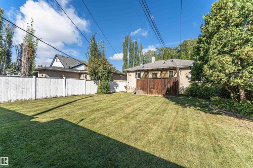 Expansive lawn area with a white privacy fence, mature trees, and a property exterior featuring stucco siding and wood paneling - 8743 Strathearn Drive Nw, Edmonton, AB 