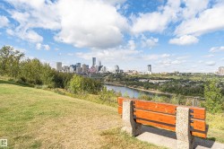Expansive green space with a wood and stone park bench, offering a panoramic cityscape across the river - 