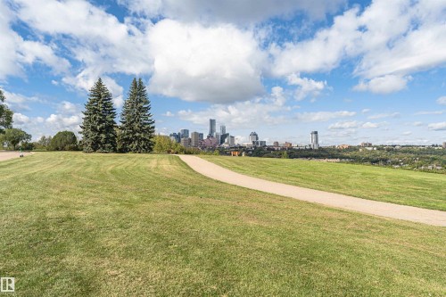 Expansive green space with a paved walking path, mature evergreen trees, and a distant city skyline - 8743 Strathearn Drive Nw, Edmonton, AB 