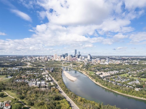 Aerial perspective of a city skyline with multiple high-rise structures, a wide river with an exposed sandbar, and extensive green spaces - 8743 Strathearn Drive Nw, Edmonton, AB 