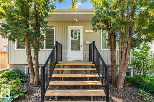 Vertical siding exterior with stone veneer accents, wood-finish steps with dark railing, and established landscaping - 8743 Strathearn Drive Nw, Edmonton, AB 