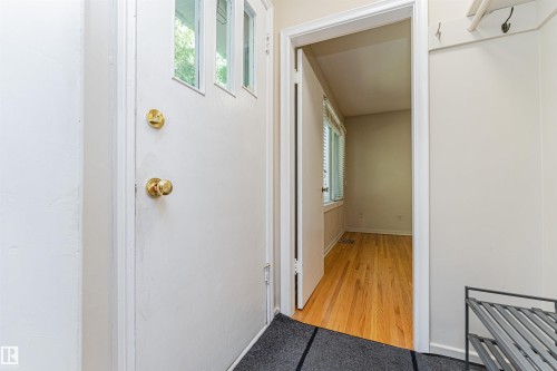 Entryway featuring a white door with transom-style windows and brass hardware, hardwood flooring, and a built-in coat rack - 8743 Strathearn Drive Nw, Edmonton, AB 