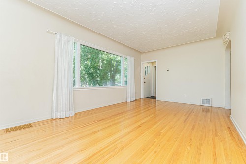 Hardwood flooring, expansive window, arched doorway with decorative molding, and neutral wall tones - 8743 Strathearn Drive Nw, Edmonton, AB 